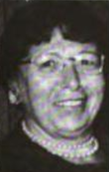 A smiling middle-aged white woman with dark hair, wearing glasses and two strands of pearls