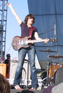 Brownstein playing guitar onstage, lifting her arm above her head in a windmill fashion