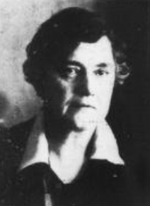 A middle-aged white woman with short dark greying hair, wearing a dark top or jacket with a white collar