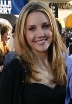 Head shot of a smiling Bynes, a camera and people in the background.