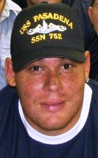 Posed neck-up photograph of Miller looking at the camera wearing a USS Pasadena baseball cap and a diamond stud in his left ear.