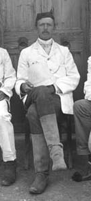 Black-and-white photograph of a man in a white shirt and dark trousers, seated, facing the camera