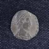 A small silver coin mostly consisting of a human head and shoulders. The shape is irregular and there is only a vestige of writing.