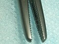 Close-up of a needle driver showing the cross-serrated teeth of its jaws