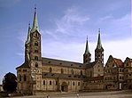 A stone cathedral with two towers on the west façade and two towers flanking the choir, all four towers are topped with slender, pointed metal roofs.