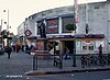 A grey-bricked building with a rectangular, dark blue sign reading "TOOTING BROADWAY STATION" in white letters all under a grey sky