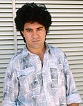 Pedro Almodóvar with black hair, wearing a bright shirt and looking to the front