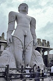 Giant grey stone statue of nude man with vines climbing legs to his arms