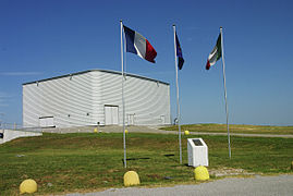 A square, white, windowless building with three flags in front