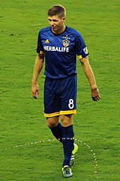 Garrard walking across a pitch in a dark blue kit with yellow trimming