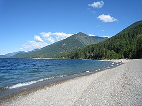 A pebble beach along a lake with a tree-covered mountain in the background