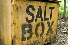 A three-quarters view of a wooden box, painted safety yellow with black letters on the front panel which read salt box in all capital black letters.