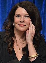 A photograph of a woman with long hair and dark-colored clothes.