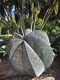 Una escultura de cobre que se comprende de siete segmentos forjados de un cable ondulado de cobre, parado detrás de un grupo de palmeras