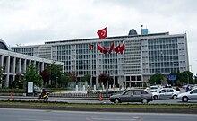 A mid-rise glass-paned office building, with an array of Turkish flags in the front.