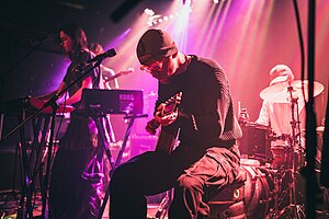 Part of a band playing music under pink lighting.