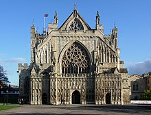 The facade of Exeter Cathedral appears to have been constructed in three layers. In the first layer there is the gable of the cathedral with a traceried window which peeps over the battlements of the second layer. This layer, which is battlemented, includes the lower aisles and a large western window which has within its arch a circular pattern of elaborate stone lace. Across the entire lower front of the building stretches a stone screen with three doors into the nave and the aisles. The screen is tiered with niches containing numerous statues.