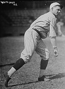 A man wearing a pinstriped baseball uniform standing and turned to his left having just thrown a baseball