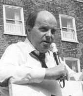 middle-aged man, bald, speaking into a microphone