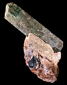 Fluorapatite: Long prism-like crystal, without luster, at an angle coming out of aggregate-like rock