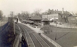 Double railroad tracks beneath street level with a multistory station building and business district to one side