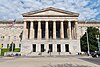 A 3-story building. The first story is granite, while the second two are sandstone. There is a pedimented front with columns spanning the second and third floors and the entrance on the first.