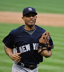 Mariano Rivera jogging on a baseball field wearing a baseball glove and navy blue hat and baseball jersey.