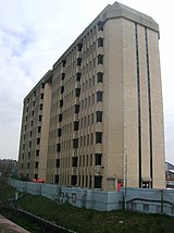 A nine-storey concrete office building sits behind a blue-painted retaining wall beside a railway cutting.