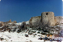 Ruins of the tower and the walls of a fortress made of stone on a hill covered with snow