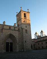 Portada del Evangelio y torre del campanario, con las torres de la Iglesia de San Francisco Javier al fondo.