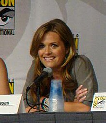 A woman in a grey shirt sitting behind a microphone