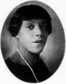 A Black woman with hair cut in a bob with bangs, wearing a strand of pearls, in an oval frame