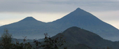 Photograph of Mts. Gahinga and Muhabura, silhoutted against the dusk sky, with another smaller hill visible in the foreground