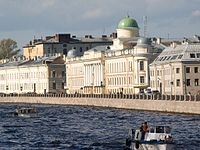 A row of large, stone three-story buildings alongside a large riverbank.