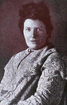 A portrait of a white woman with dark hair, wearing a printed garment.