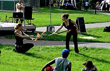 Two young persons seated on the ground watching two women dancing with fire