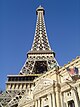 Ground-level view of a steel tower; the tower is broad at its base, rising from four separate legs. It then tapers, with each leg meeting to form a single, latticework column. Three platforms are visible at various heights up the side of the structure.