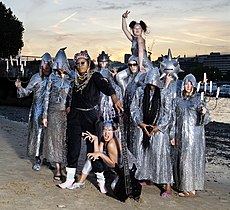 Chrome Hoof on a dawn/dusk Summer of 2007 river beach, dressed to promote 'Pre-Emptive False Rapture'. Flanking members hold candelabra and most are wearing silvery cowls, with Shingai Shoniwa counterpointed in matt black.