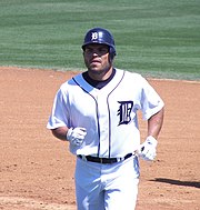 Man in a white baseball uniform and navy-blue helmet jogs on a baseball field