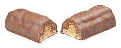 A candy bar with peanut butter, roasted peanuts and caramel coated in milk chocolate, broken in half at the middle to show the interior of the bar