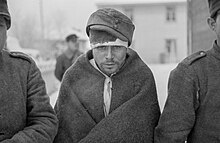 Soviet prisoners of war keep warm with their new clothes. The prisoner in the middle of the photo is staring at the ground with hollow eyes.