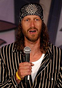 A man with long hair speaking into a microphone.