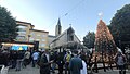 la plaza un dia de concierto navideña. se puede observar entre la gente el arbol con luces, pesebre, la catedral y edificio correos detras