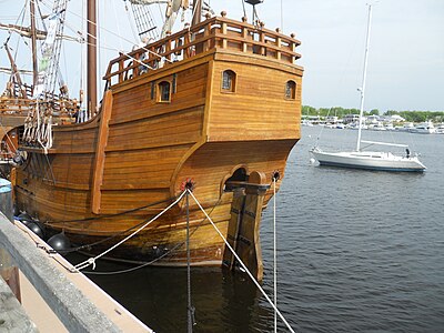 View of the stern. The deck at the top is the poop deck. Just below it is the cabin, which has windows. The door exits to the quarterdeck, which ends with a drop to amidships. The tiller fastened to the top of the rudder enters the vessel.