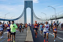 Multiple people running towards the camera, with suspension bridge in background