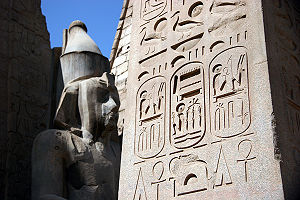 Inscribed hieroglyphics cover an obelisk in foreground. A stone statue is in background.