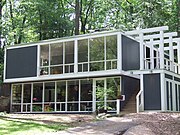 A two-level, slightly larger No. 5 house, painted gray with white window trim that was built into the slope on a cinder-block base.