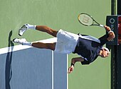 Raonic with both feet in the air at the service line, his racquet behind him, and his eyes looking up.