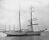 View of a brigantine rigged two-masted sailing ship at anchor with sails furled, a raised observation deck is visible between the two masts