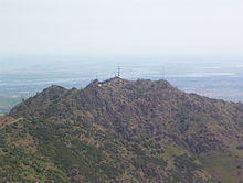 A rocky, partially forested mountain peak with several communications antennas